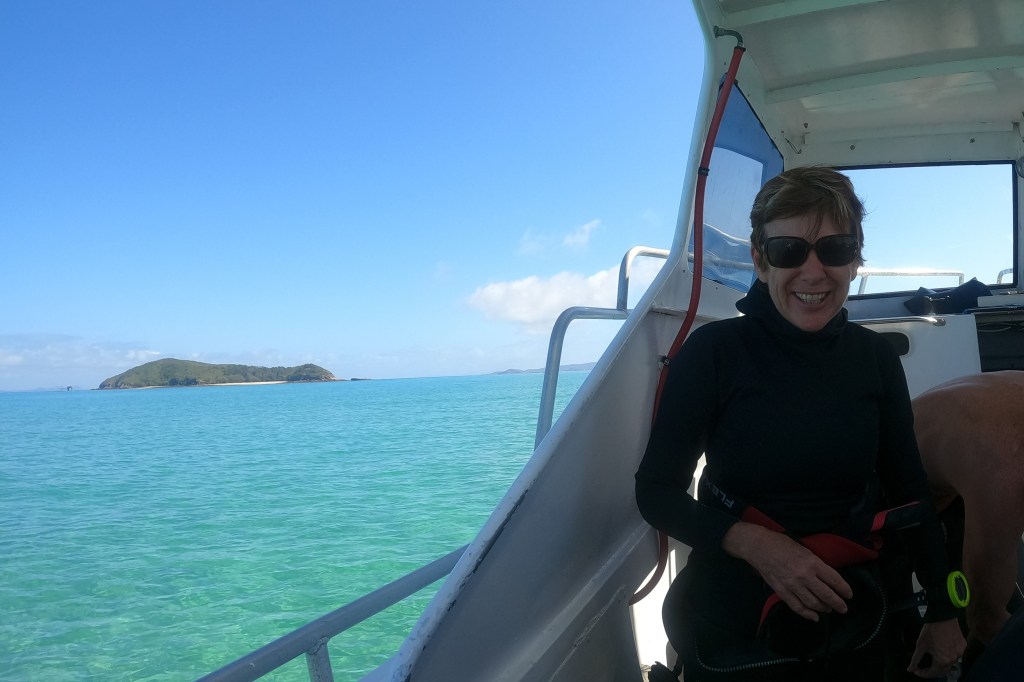 Woman diver on a boat with an island in the background EMPTY NEST DIVER