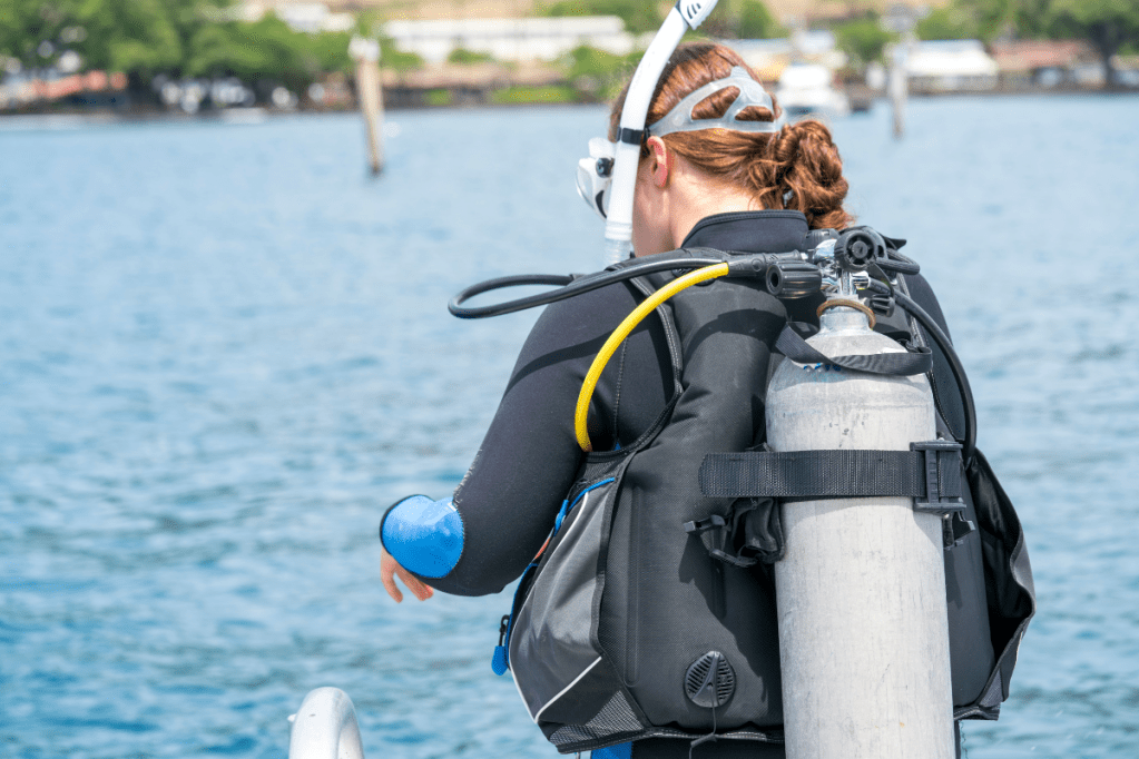 Woman scuba diver overlooking water with tank on her back