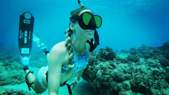 A woman underwater with a mask and snorkel and a ponytail held with mermaid ties