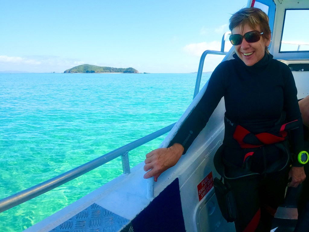 A Scuba Woman, Empty Nest Diver on a dive boat with an island in the background.