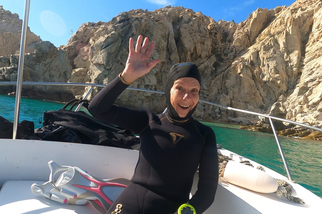 A Scuba Woman wearing a wetsuit and hood waving
emptynestdiver.com